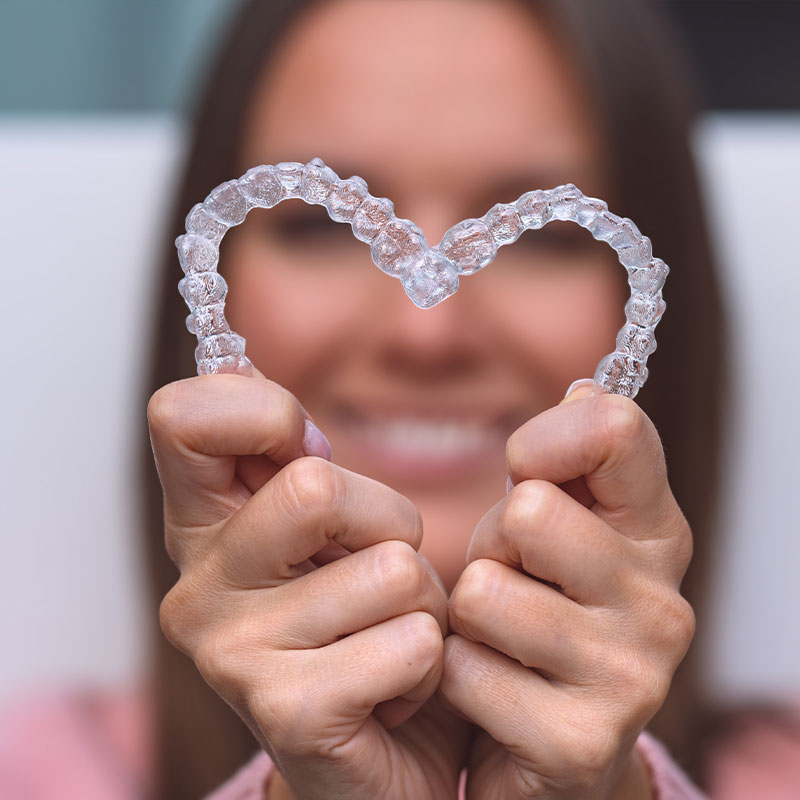 The image shows a person holding up a heart-shaped object with their hands, smiling at the camera.