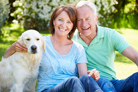 An elderly couple sitting on grass with a golden retriever between them.
